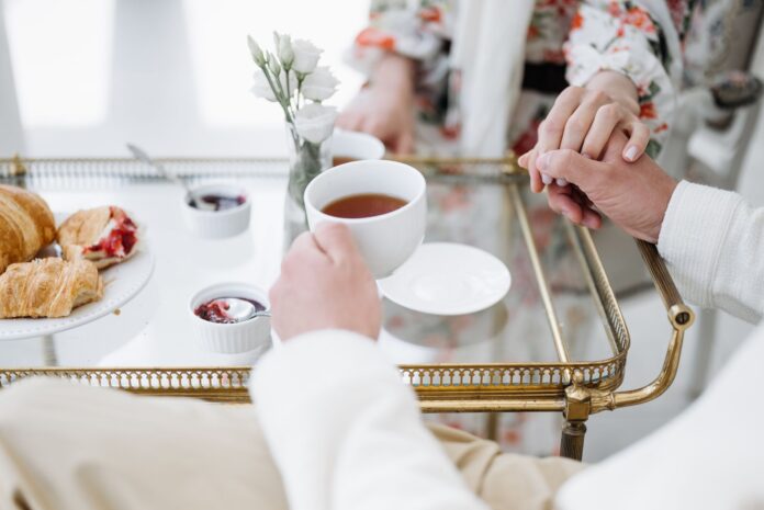Eleganckie śniadanie we dwoje z herbatą, wypiekami i splecionymi dłońmi Eleganckie śniadanie we dwoje z herbatą, wypiekami i splecionymi dłońmi
